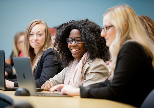 Three female students dressed professionally at a desk in a classroom. 
