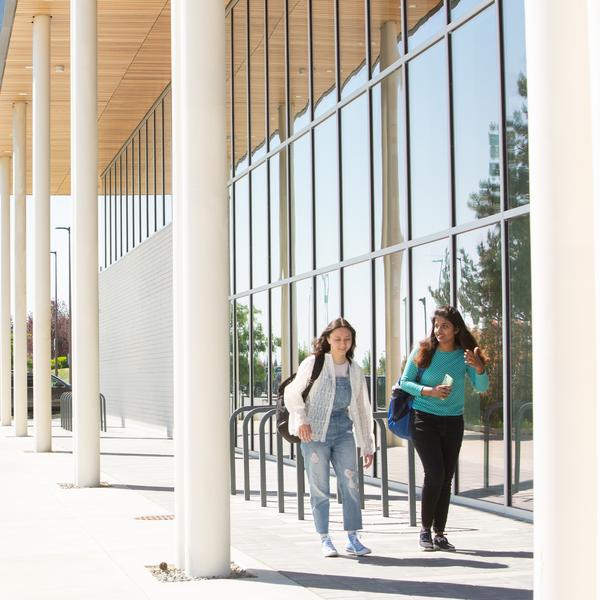 two students walking by a building with mirrored windows. 