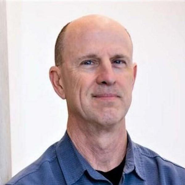 A man smiling in a blue collared shirt. 
