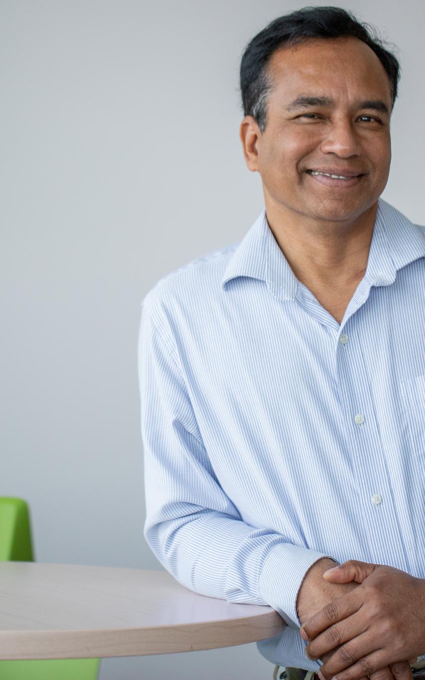 A man with short dark hair in a dress shirt leaning on a tall table. 
